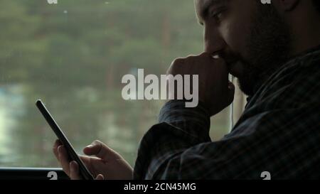 Young concentrated man making money transaction via application on mobile phone in a train. Stock Photo