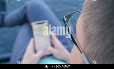 Man using his smartphone writing a message sitting on a bench. Stock Photo