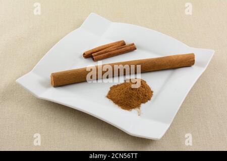 Dutch cinnamon stick snack with cinnamon stick and pile of ground cinnamon on white snack plate on light brown tablecloth Stock Photo