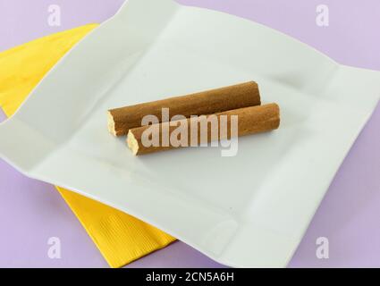 Dutch cinnamon stick snack halves on white snack plate with yellow napkin on lavender background Stock Photo