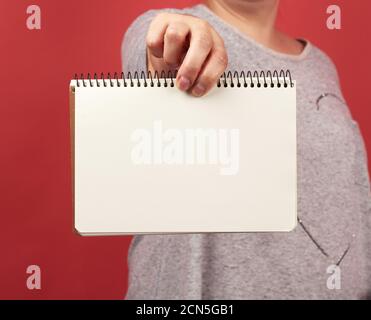 woman in gray clothes holding an open spiral notebook in front of her with empty white sheets, red b Stock Photo
