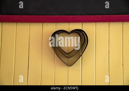 Three heart shaped cake tins hanging on a vintage timber wall as a decorative display item Stock Photo