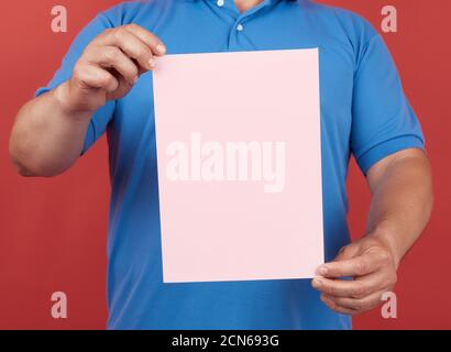 man in blue clothes holds an empty sheet of pink paper on a red background Stock Photo