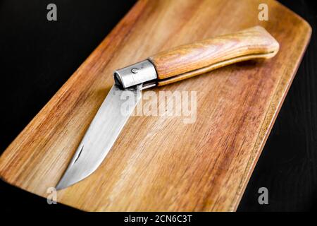 Wooden cutting board and pocket knife on a black table Stock Photo