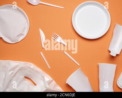 used plastic dishes, pieces of plastic and a white plastic bag on an orange background Stock Photo