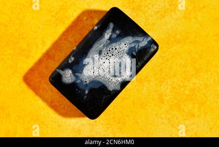 Wet bar of black soap with bubbles on yellow bright background Stock Photo