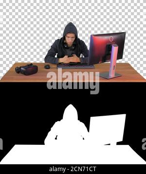 Hooded hacker using laptop and smartphone, Alpha Channel with Si Stock Photo