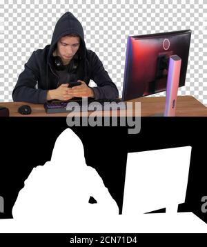 Hooded hacker using laptop and smartphone, Alpha Channel with Si Stock Photo