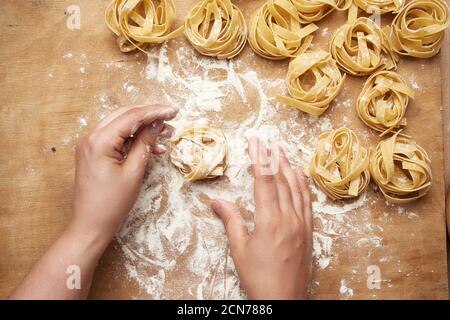 raw fettuccine pasta and two female hands are cooking pasta on a brown wooden table Stock Photo