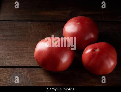 three ripe red tomatoes on a brown wooden background Stock Photo