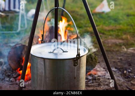 Camping bowler hat hangs over the fire on a tripod Stock Photo