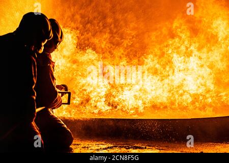 Firefighters use twirl water fog spraying down fire flame. Stock Photo