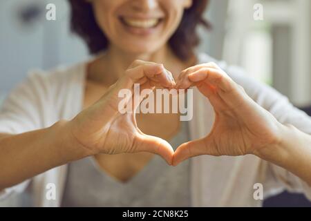Cropped shallow focus image of happy smiling lady showing heart symbol with her hands Stock Photo