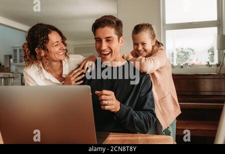 Family making video call while at home. Couple with their daughter sitting in front of laptop making a video call. Stock Photo