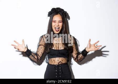 Woman screaming and looking scary in her halloween witch costume, spread hands sideways and looking angry, trying scare people during trick or treat Stock Photo