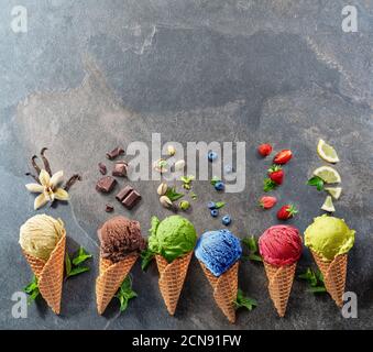 Set of various colorful ice creams in waffle cones with fruits slices on the grey background. Top view. Stock Photo