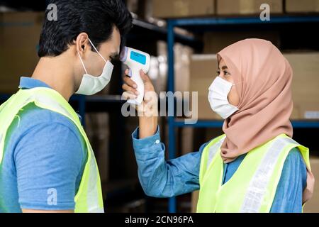 Islam Muslim asian warehouse worker take temperature to another worker Stock Photo
