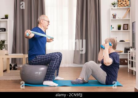 Senior couple exercising in living room using yoga mat and stability ball. Old person healthy lifestyle exercise at home, workout and training, sport activity at home on yoga mat. Stock Photo