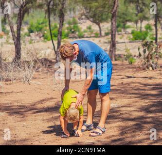 Sport father son exercising in forest park fresh air, workout enjoying together, squatting and side bend technique, wear face blue mask protect Stock Photo
