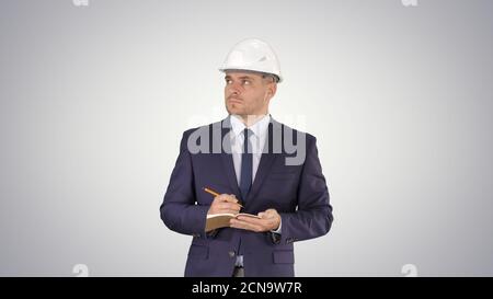 Engineer in suit and helmet walking and writing notes in notepad Stock Photo