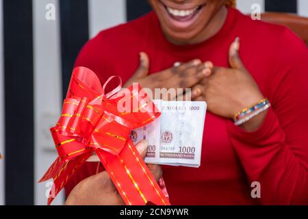 lady expresses her surprise when someone shows her some money wrapped with a red ribbon as a gift Stock Photo
