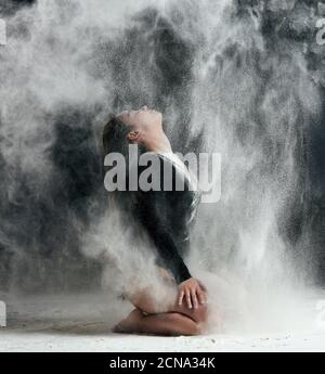aucasian woman with long hair is dressed in a sports black bodysuit and sits on the floor and throwi Stock Photo