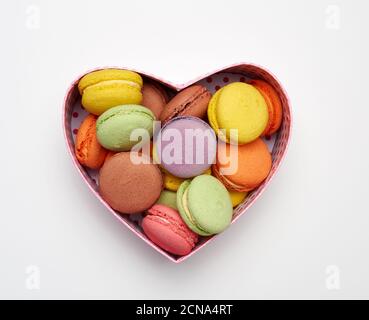 round baked multicolored macarons lie in a red cardboard box in the shape of a heart Stock Photo