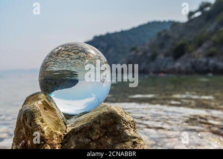 Crystal ball on stones near the sea. Original upside down view and rounded perspective of the sky and pebble seabed. Original and engaging picture. Stock Photo