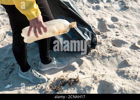 Woman picking up trash and plastics cleaning the beach with a garbage bag. Environmental volunteer activist against climate change and the pollution o Stock Photo