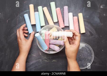 multicolored chalk in a plastic bucket on a black background, female hands fold objects into a conta Stock Photo
