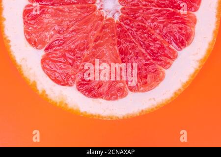 Slice of half red grapefruit on orange background, juicy citrus section texture. Abstract summer wallpaper, bright tropical pattern. Healthy food conc Stock Photo