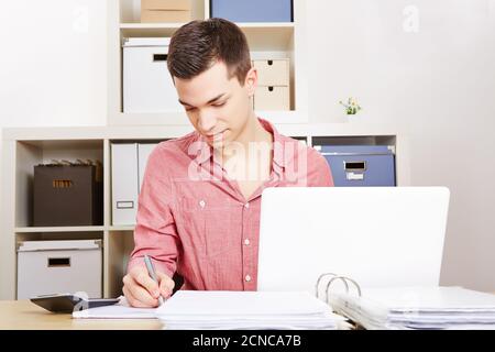 Young man works on computer in office and takes notes Stock Photo