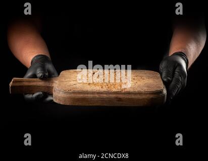 two male hands in black latex gloves hold an empty vintage brown wooden chopping board Stock Photo