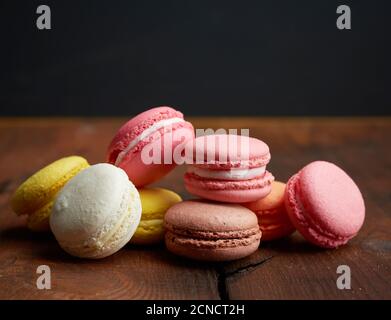 baked multi-colored macarons cookies lie in a row on a brown wooden background Stock Photo