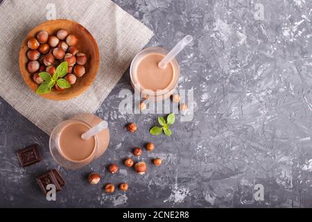 Organic non dairy hazelnut chocolate milk in glass and wooden plate with hazelnuts on a gray concrete background. Vegan healthy food concept, flat lay Stock Photo