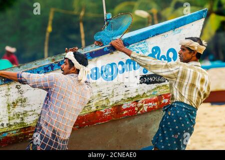 Fishermen pulling heavy old boat on to shore at busy, popular Marari Beach, Mararikulam, Alappuzha (Alleppey), Kerala, India, Asia Stock Photo