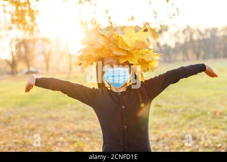 Little girl wearing medical face mask prevent pollution on fallen leaves at park. Stock Photo