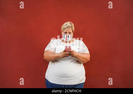 Curvy woman using smartphone outdoor wearing face protective mask - Coronavirus lifestyle concept Stock Photo