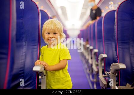 Toddler boy, child boarding on the airplane, standing on the aisle between the rows of seats, smiling happily Stock Photo