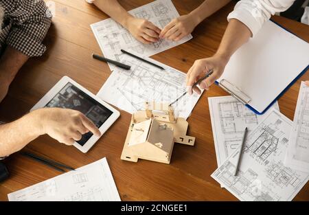 Top view hands of architect-engineer and young couple during presentation of future house. Top view table with documents, blueprint. First home, industrial, building concept. Moving to new live place. Stock Photo