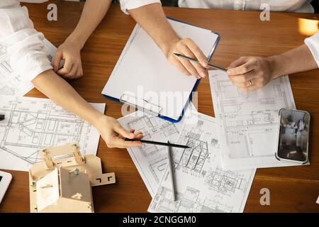 Top view hands of architect-engineer and young couple during presentation of future house. Top view table with documents, blueprint. First home, industrial, building concept. Moving to new live place. Stock Photo