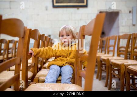 Little toddler boy, praying in chapel with candles in front of him Stock Photo