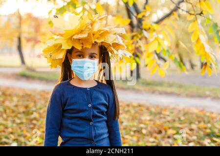 Little girl wearing medical face mask prevent pollution on fallen leaves at park. Stock Photo