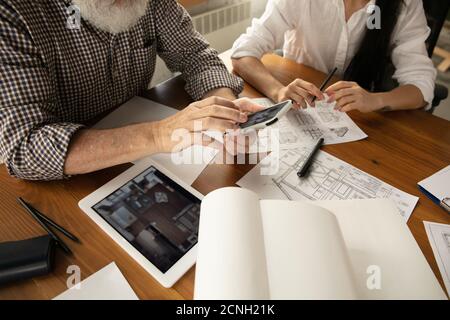 Top view hands of architect-engineer and young couple during presentation of future house. Top view table with documents, blueprint. First home, industrial, building concept. Moving to new live place. Stock Photo