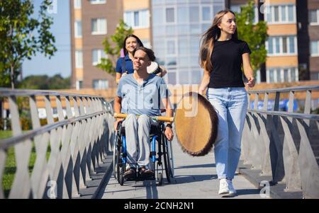 Emotions. Happy handicapped man on a wheelchair spending time with friends playing live instrumental music outdoors. Concept of social life, friendship, possibilities, inclusion, diversity. Stock Photo