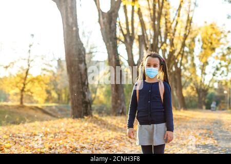 Little girl wearing medical face mask prevent pollution on fallen leaves at park. Stock Photo