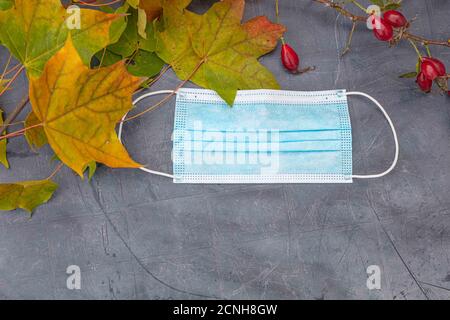 yellow maple leaves, rose hips and a medical mask lie on a gray plastic table concept, protect yourself from coronavirus. High quality photo Stock Photo