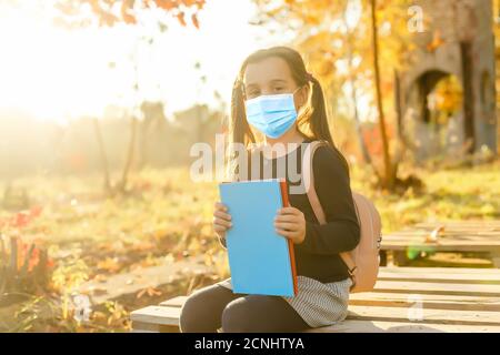 Little girl wearing medical face mask prevent pollution on fallen leaves at park. Stock Photo