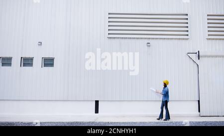 Beautiful Asian female engineer in jeans dress wearing yellow safety hard hat doing job at construction site outside office. Idea for modern working w Stock Photo