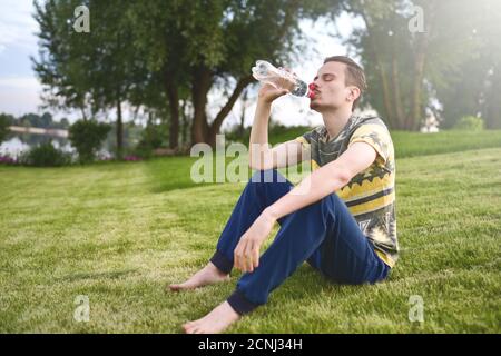 Young man sitting on the garden and drinking water after running.summer time. recreation concept Stock Photo
